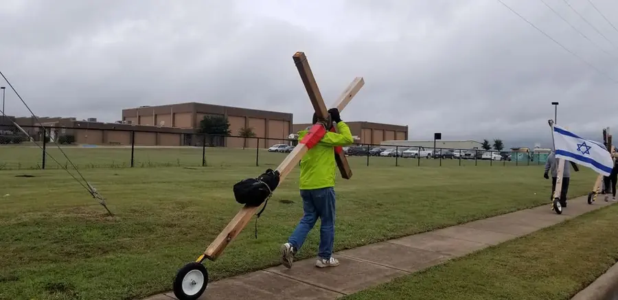Cross Made Me Ministries volunteer carrying a wheeled wooden cross across a field during a community cross walk