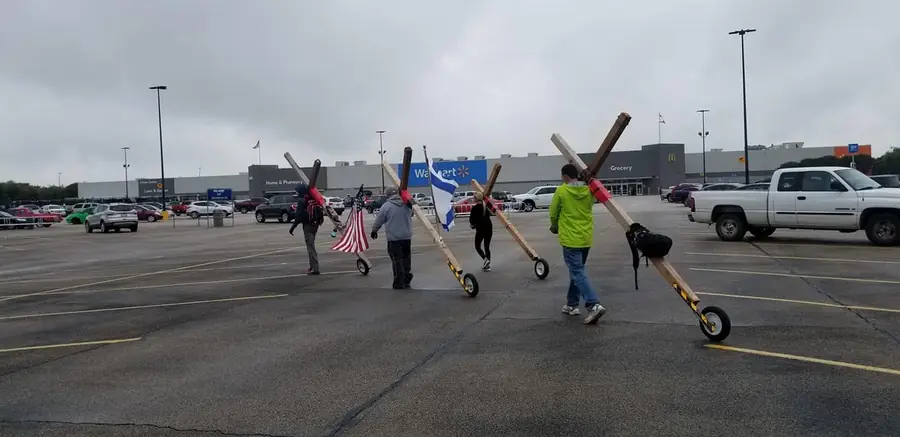 Group of volunteers carrying wheeled crosses and flags across a parking lot during an outreach cross walk